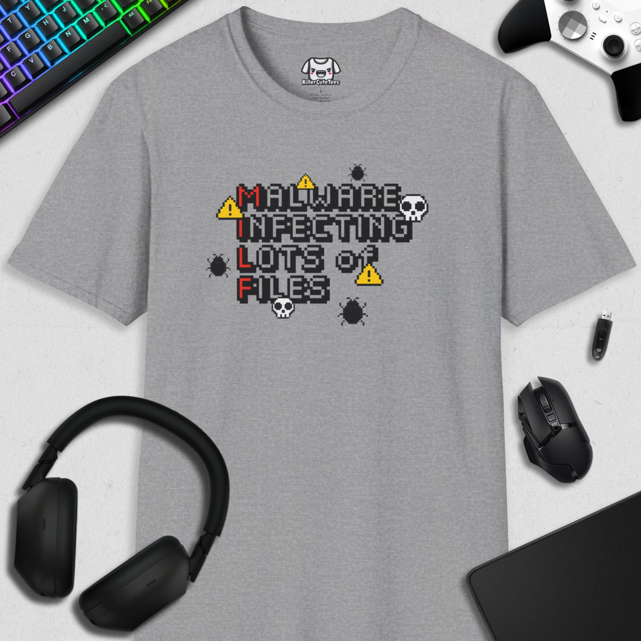 Gray t-shirt with pixelated text 'MALWARE INFECTING LOTS OF FILES' on a white surface with gaming accessories.