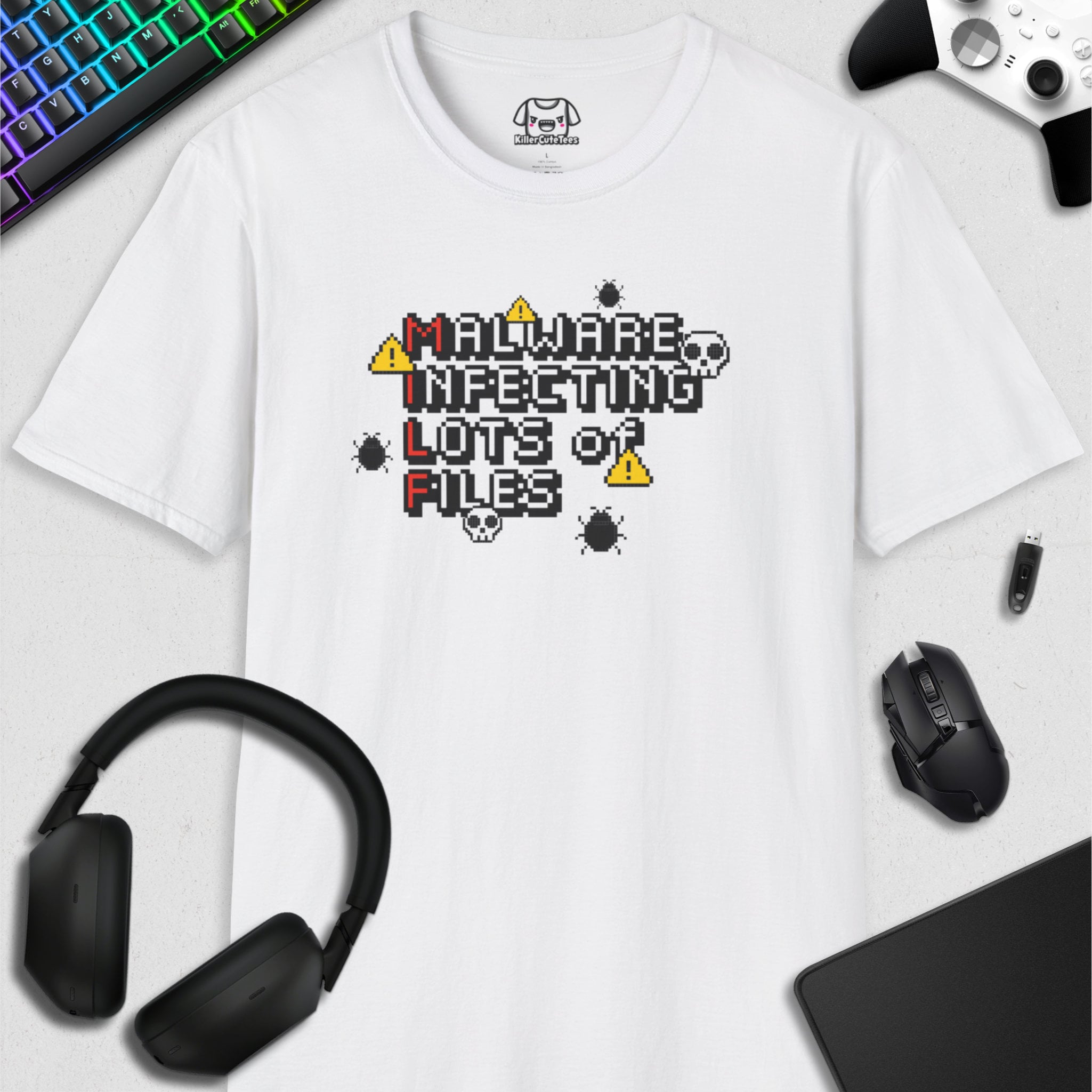 White t-shirt with 'Malware Infecting Lots of Files' graphic design, surrounded by gaming accessories on a light gray background.