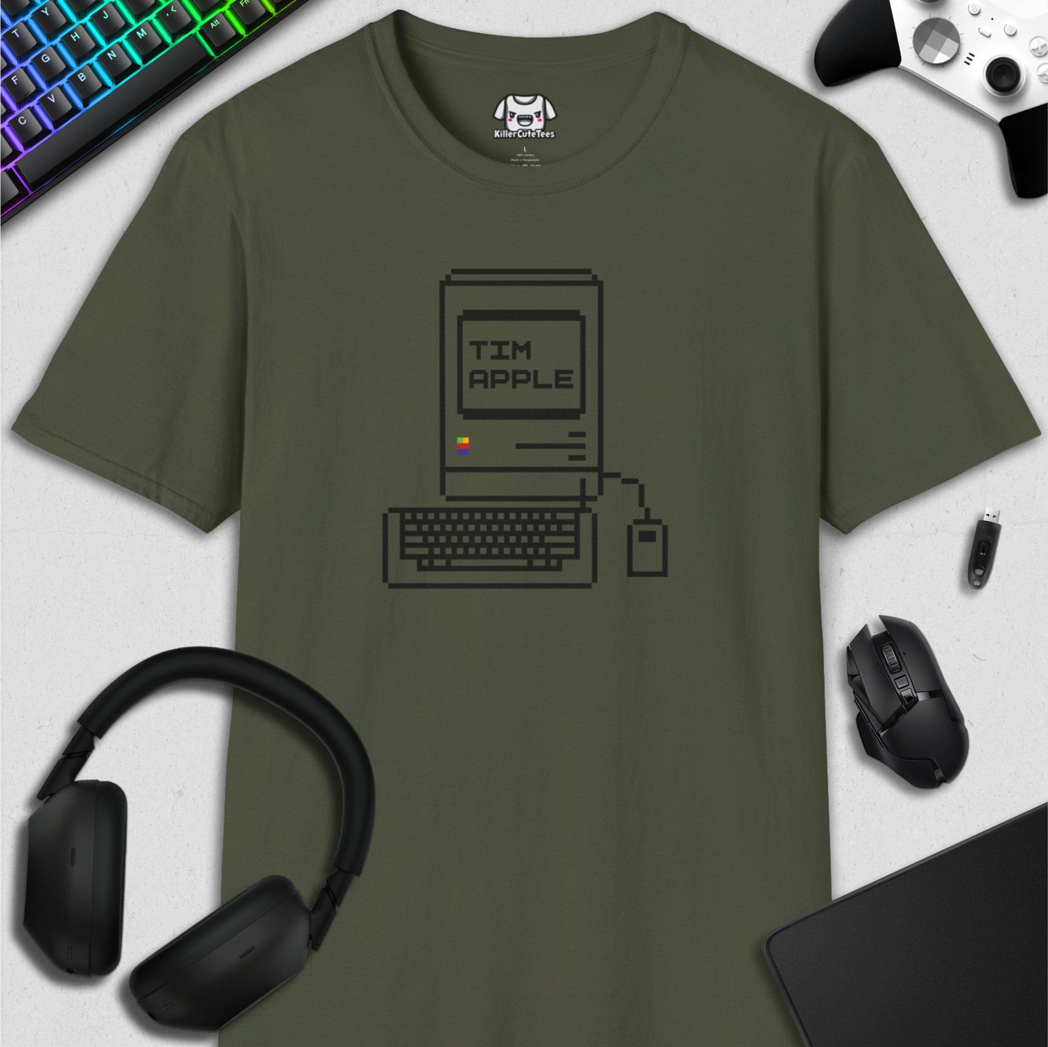Green t-shirt with computer graphic and 'TIM APPLE' text, surrounded by tech accessories on a light gray background