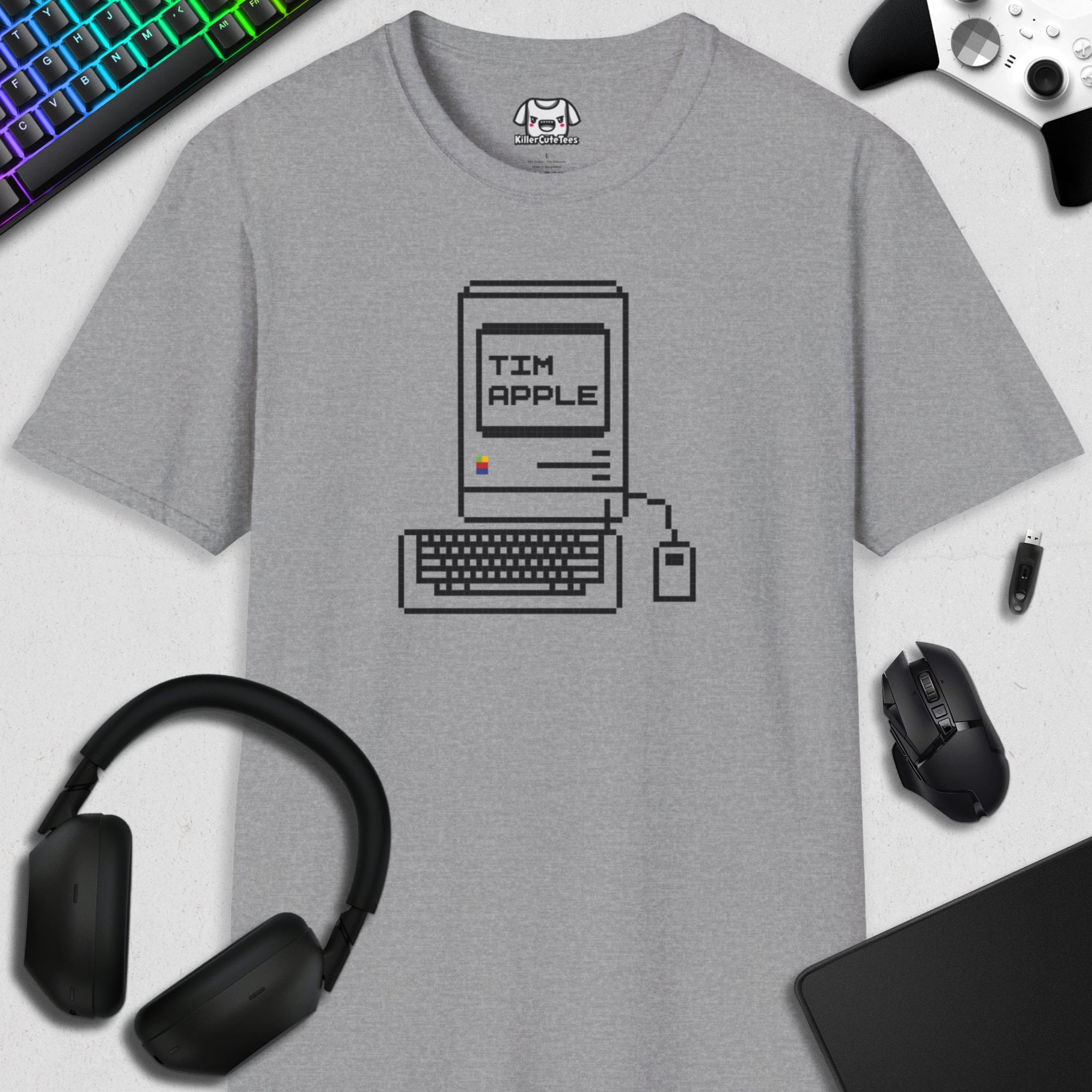 Gray t-shirt with computer graphic design on a white surface with tech accessories.