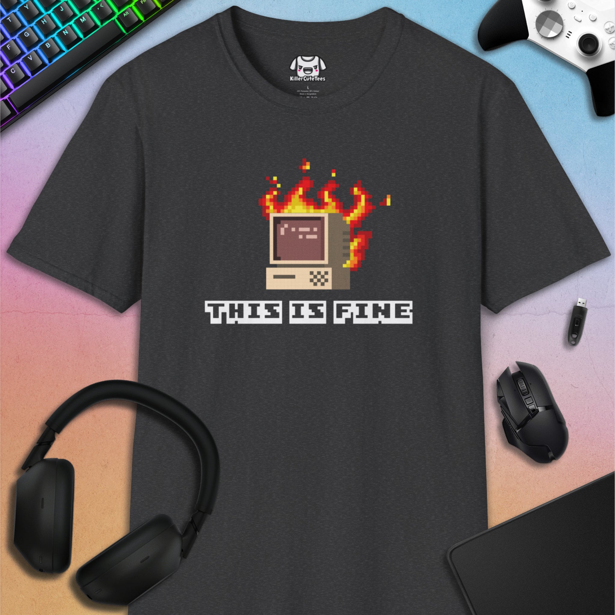 Black t-shirt with pixel art design and 'This is Fine' text, surrounded by gaming accessories on a gradient background.