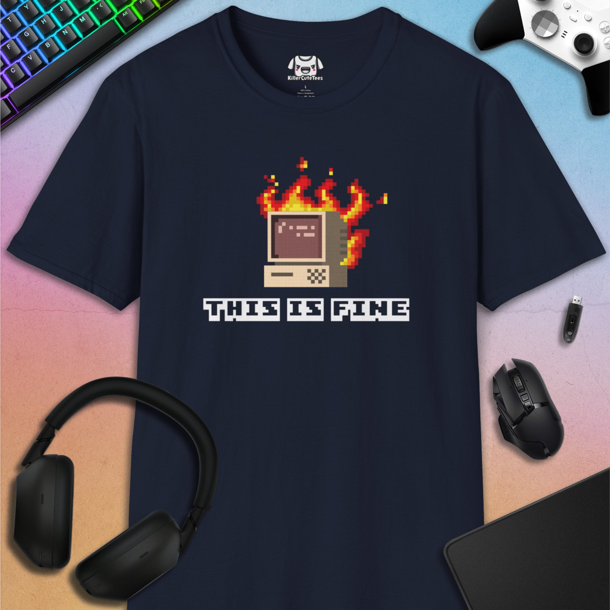 Black t-shirt with pixelated computer graphic and 'This is Fine' text on a colorful desk setup.