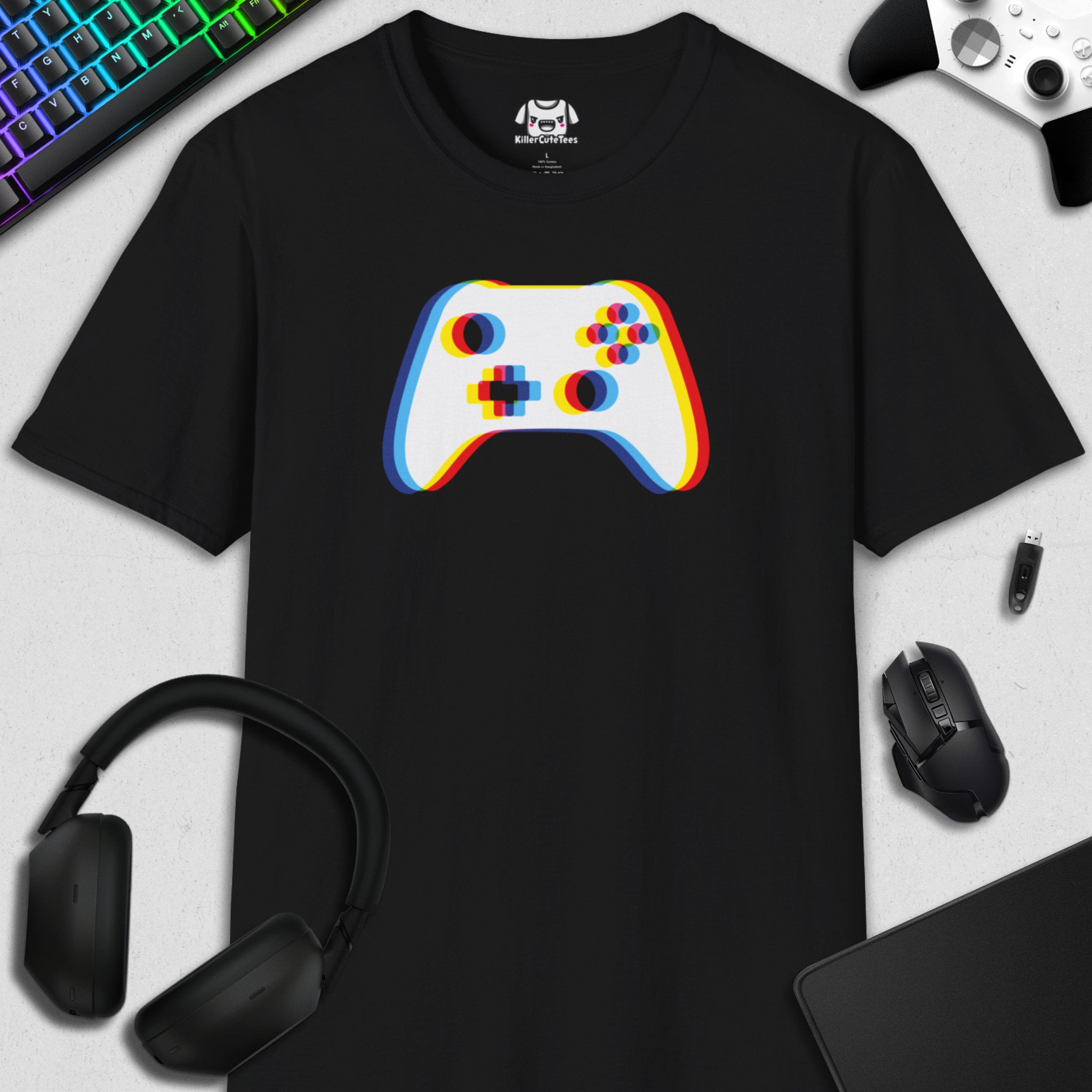 Black t-shirt with a colorful gaming controller design on a desk with gaming accessories.